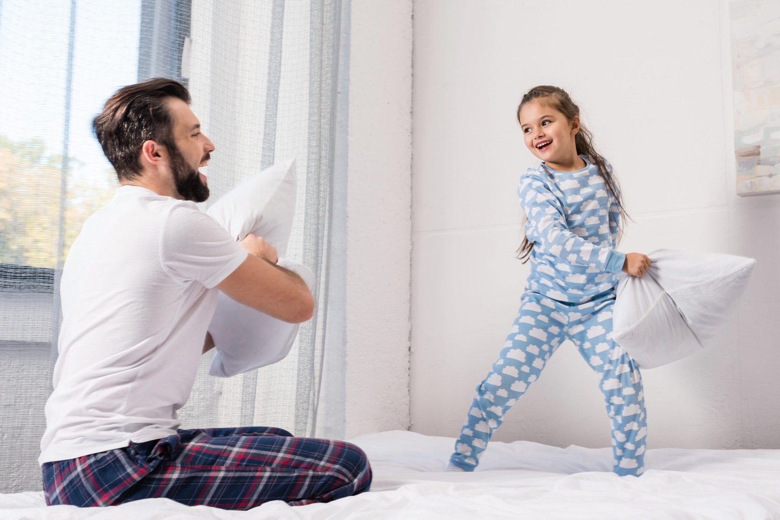 happy father and daughter fighting with pillows in bed at morning
