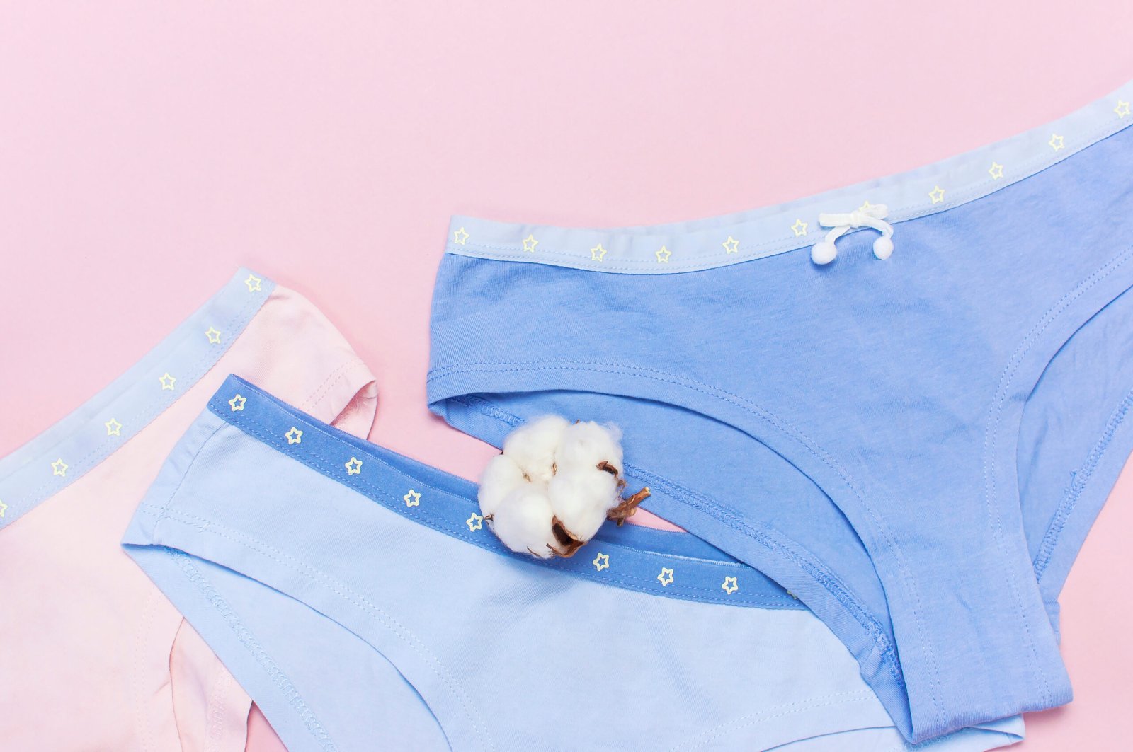 Female pastel cotton set panties and cotton flower on pink background top view flat lay with copy space for text. Fashion blog, Colorful women's natural underwear, advertising shopping concept.