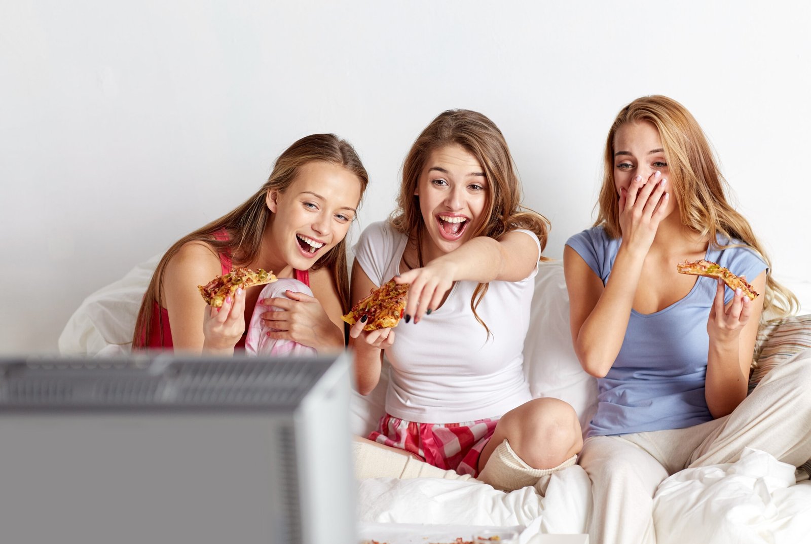 friendship, people, pajama party, entertainment and junk food concept - happy friends or teenage girls eating pizza and watching movie or tv series at home