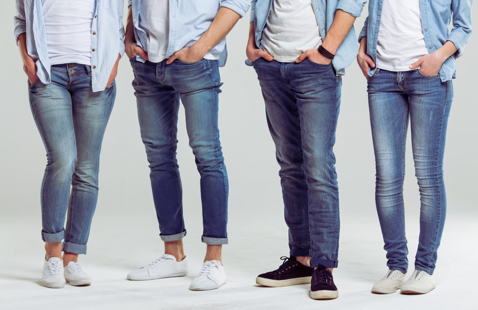 Young people in jeans standing on a gray background, legs close-up
