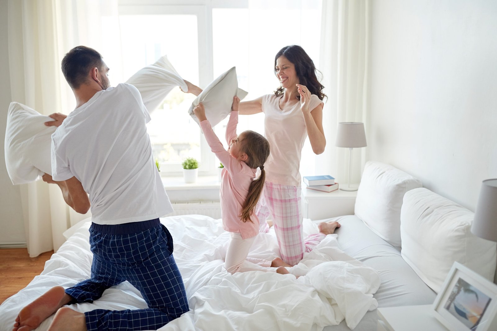 people, family and morning concept - happy child with parents having pillow fight in bed at home