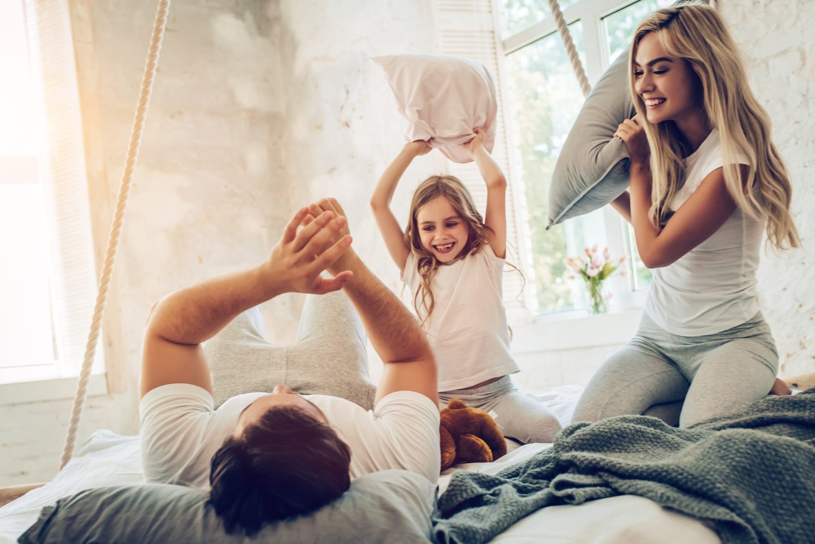 Happy family is having fun in bedroom while pillow battle. Enjoying being together.